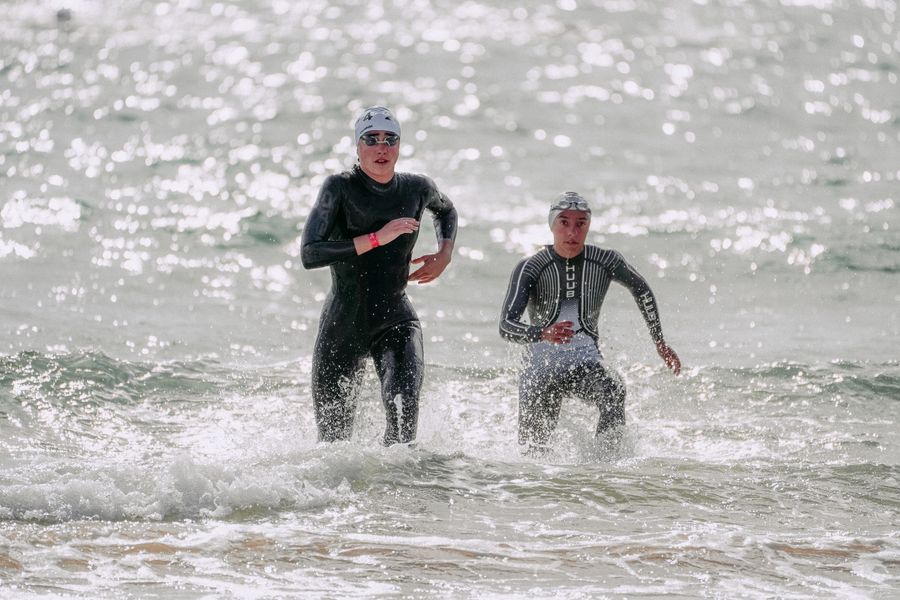 Triathletes in wetsuits running out of the water at the swim exit